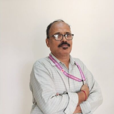 Man with glasses standing against white wall.