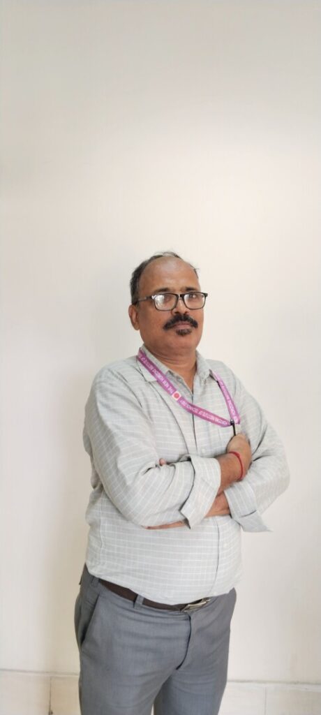 Man with glasses standing against white wall.