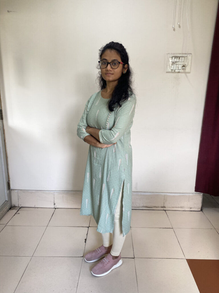 Person standing indoors, wearing glasses and green attire.