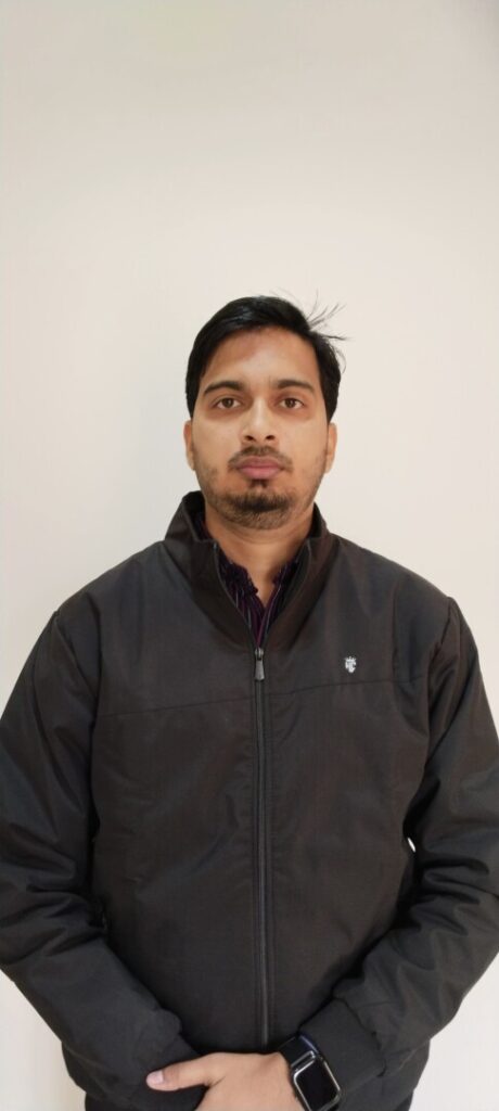 Person standing, wearing a black jacket, neutral expression.