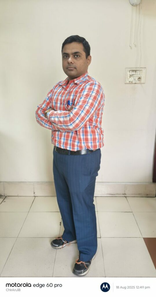 Person in plaid shirt standing indoors with arms crossed.