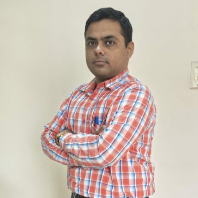 Person in plaid shirt standing indoors with arms crossed.