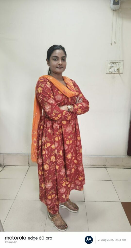 Person in red floral dress stands indoors smiling.