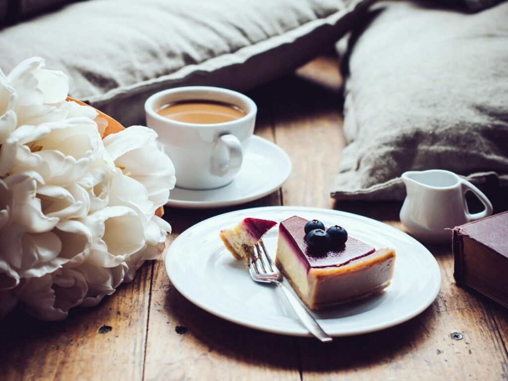 Coffee, cheesecake, and flowers on a wooden table.